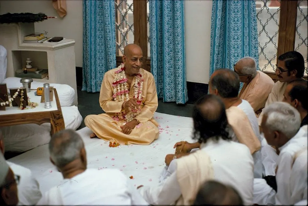 Srila Prabhupada giving darshan, seated amid rose petals
