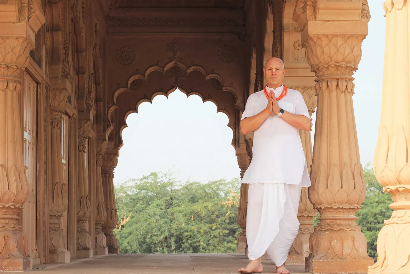 Vaisesika Dasa in pranam pose beneath an ornate temple archway
